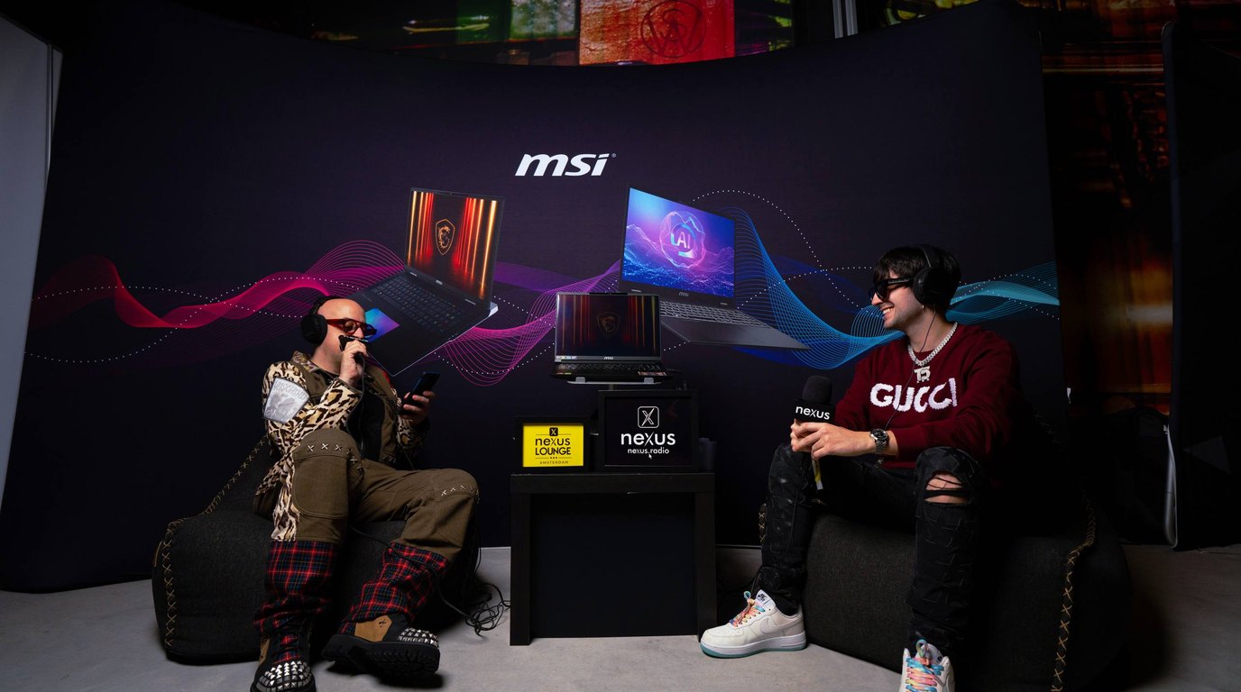 Two people talking on beanbags in front of an MSI backdrop at the Nexus Lounge, a Nexus Radio screen and microphone between them